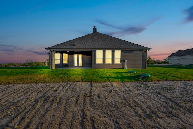 back house at dusk featuring a lawn