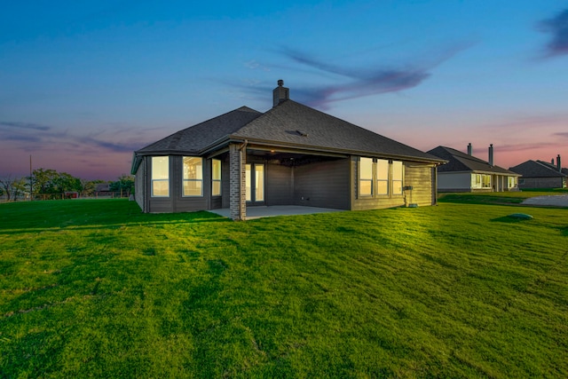 back house at dusk featuring a yard and a patio area