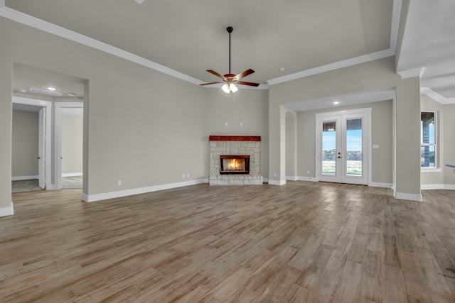 unfurnished living room featuring french doors, light hardwood / wood-style floors, ceiling fan, crown molding, and a fireplace