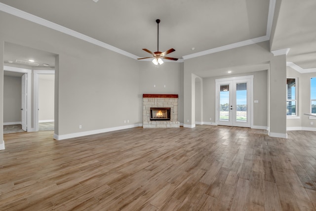 unfurnished living room featuring ceiling fan, a fireplace, crown molding, light wood-type flooring, and french doors