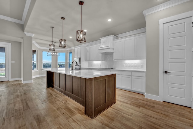 kitchen featuring backsplash, white cabinetry, a large island with sink, and light hardwood / wood-style floors