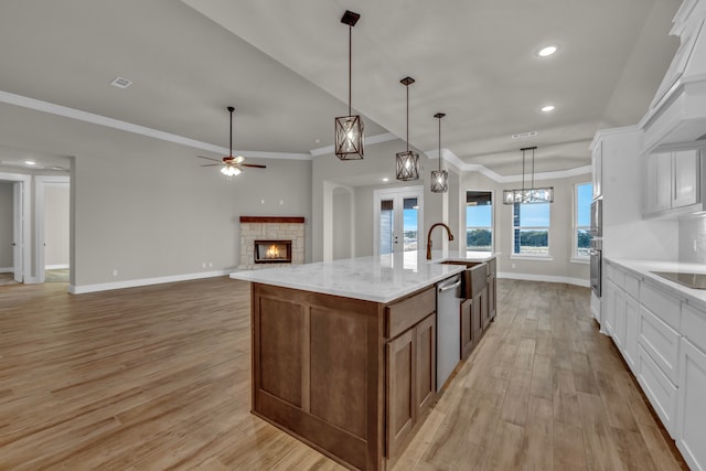 kitchen with white cabinetry, decorative light fixtures, a large island with sink, and light wood-type flooring