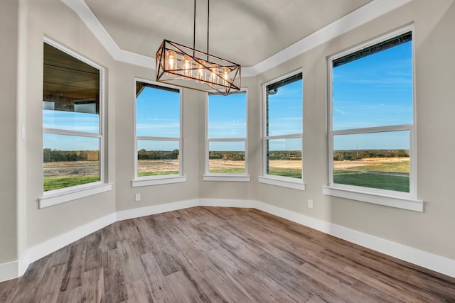 unfurnished dining area with a water view, hardwood / wood-style flooring, crown molding, and an inviting chandelier