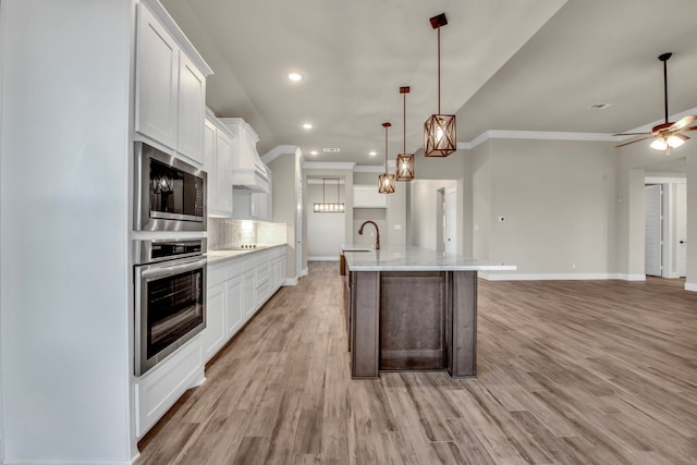 kitchen with a center island with sink, appliances with stainless steel finishes, hanging light fixtures, white cabinets, and light wood-type flooring