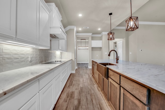 kitchen featuring light hardwood / wood-style floors, white cabinetry, sink, light stone countertops, and pendant lighting