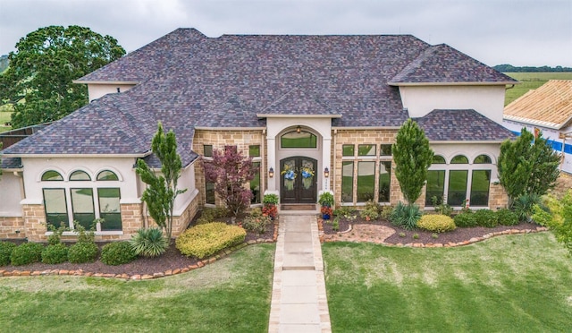 view of front of house featuring stone siding, french doors, a front lawn, and stucco siding