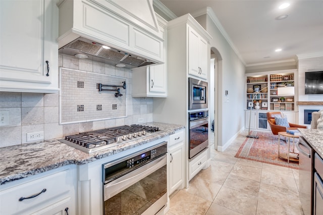 kitchen featuring light stone countertops, premium range hood, stainless steel appliances, and crown molding