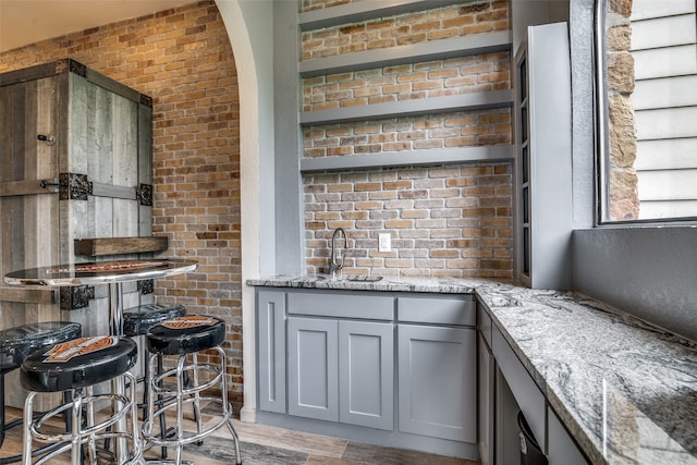 bar with gray cabinets, light stone countertops, brick wall, and sink