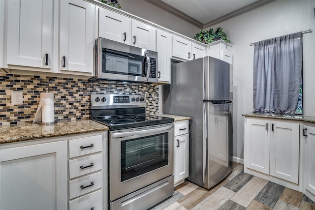 kitchen featuring appliances with stainless steel finishes, light stone countertops, white cabinets, decorative backsplash, and ornamental molding