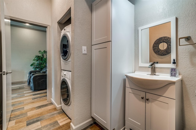 clothes washing area featuring stacked washer and dryer, sink, and light hardwood / wood-style flooring