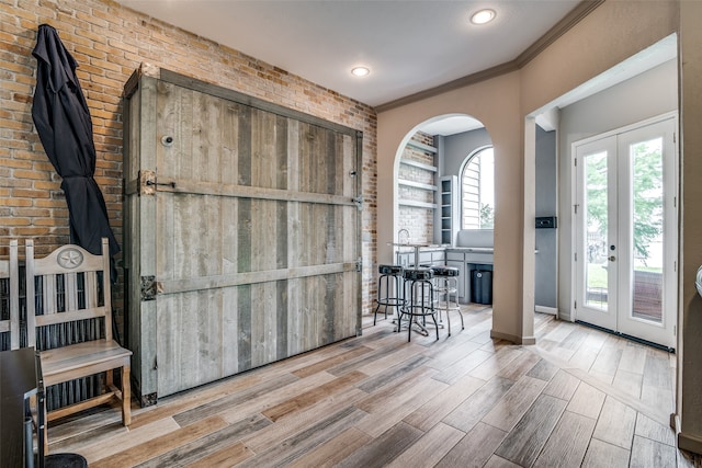 entrance foyer with brick wall, ornamental molding, french doors, and light hardwood / wood-style flooring