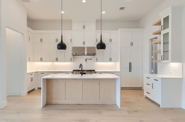 kitchen with pendant lighting, white cabinets, tasteful backsplash, a kitchen island with sink, and light wood-type flooring