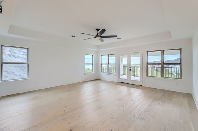 unfurnished room featuring light hardwood / wood-style floors, ceiling fan, and a raised ceiling