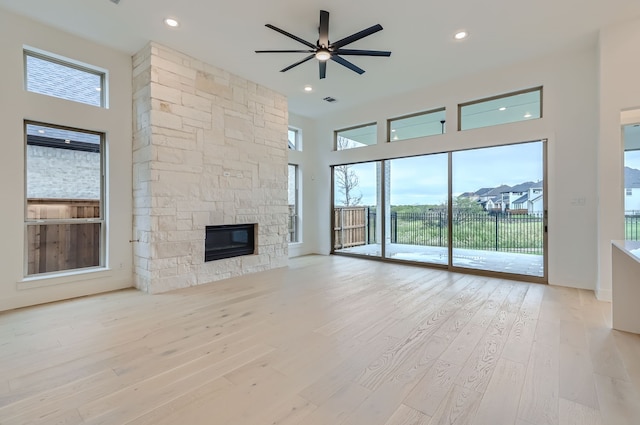 unfurnished living room featuring light hardwood / wood-style floors, a healthy amount of sunlight, a stone fireplace, and ceiling fan