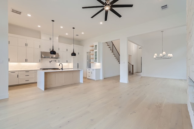 kitchen featuring white cabinets, pendant lighting, a center island with sink, ceiling fan with notable chandelier, and light hardwood / wood-style floors