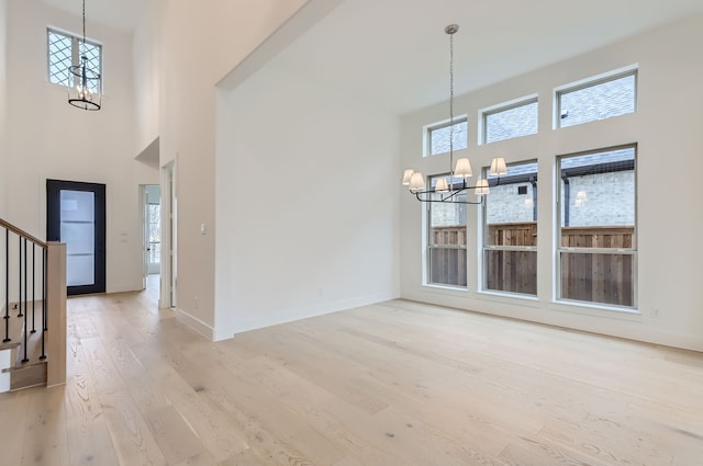 interior space with light wood-type flooring, a towering ceiling, and a chandelier