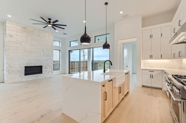 kitchen with pendant lighting, sink, an island with sink, a stone fireplace, and ceiling fan