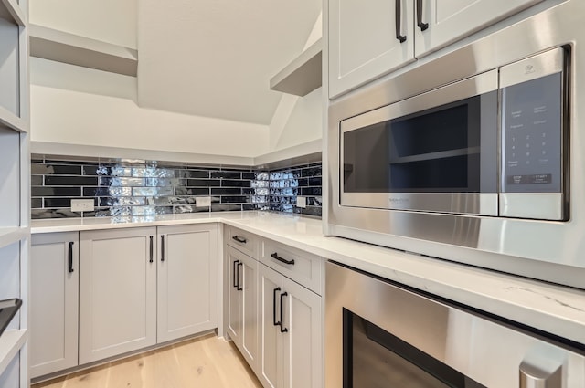 kitchen featuring light stone counters, light hardwood / wood-style floors, beverage cooler, stainless steel microwave, and decorative backsplash