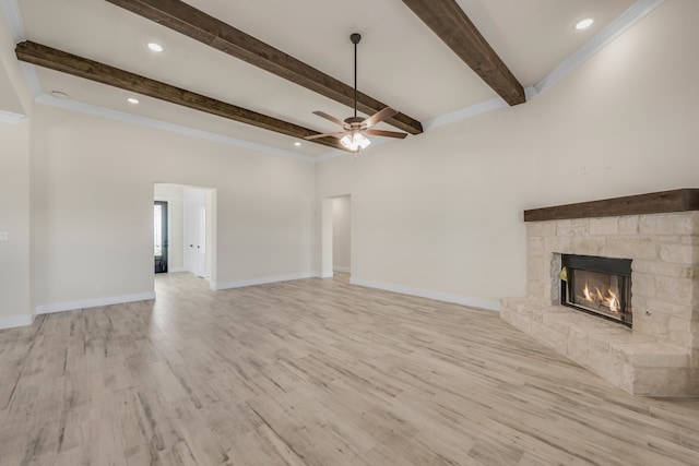 unfurnished living room with ceiling fan, a stone fireplace, beamed ceiling, and light wood-type flooring