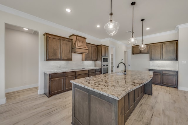 kitchen featuring an island with sink, light wood-type flooring, and decorative backsplash