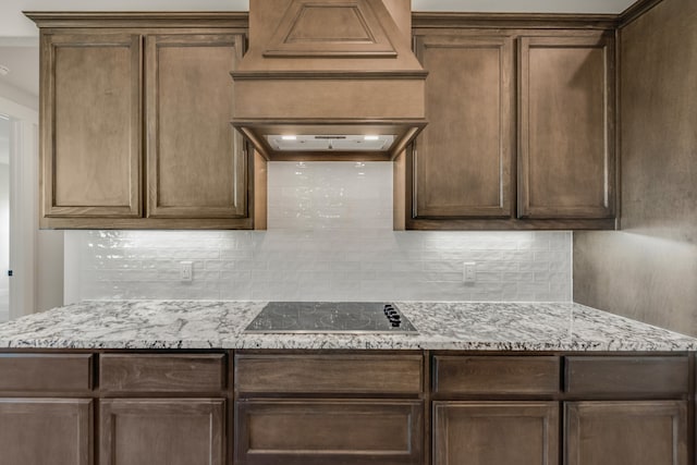 kitchen featuring light stone counters, exhaust hood, tasteful backsplash, and black electric stovetop