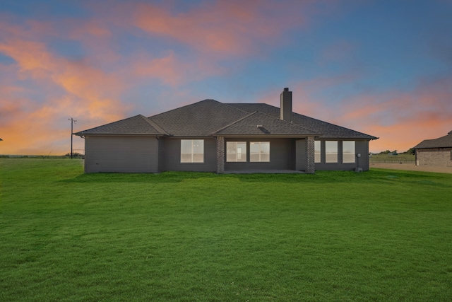 back house at dusk featuring a lawn