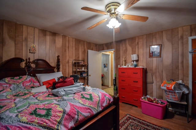 bedroom with ceiling fan, wood-type flooring, and wood walls