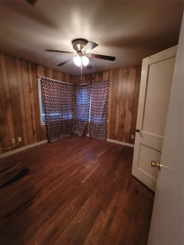 spare room featuring dark wood-type flooring, wooden walls, and ceiling fan