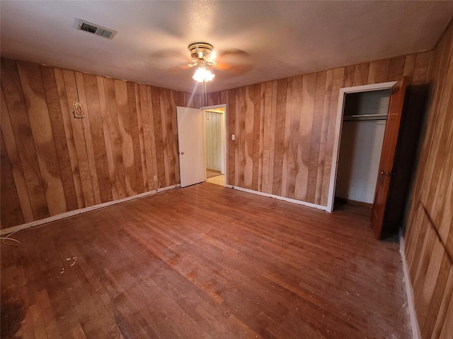 unfurnished bedroom with wood-type flooring, ceiling fan, and wood walls