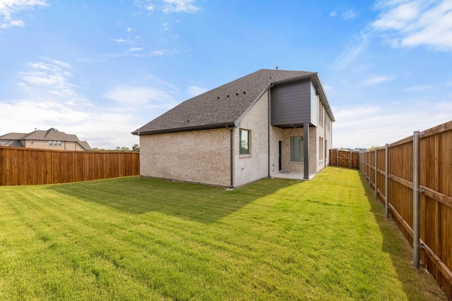 rear view of house featuring brick siding, a lawn, a shingled roof, and a fenced backyard