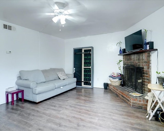 living room with wood-type flooring, ceiling fan, and a fireplace