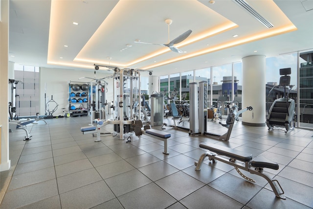 gym featuring ceiling fan, tile patterned floors, a tray ceiling, and floor to ceiling windows