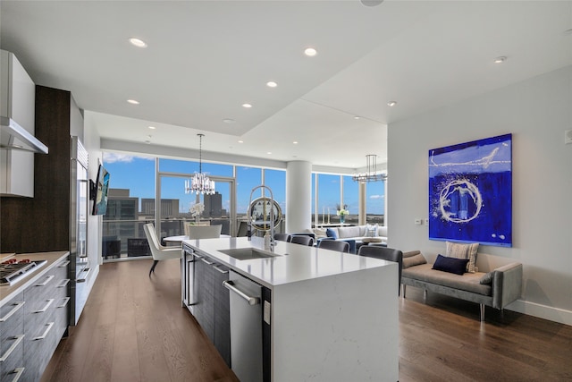 kitchen featuring stainless steel appliances, sink, a center island with sink, dark wood-type flooring, and a notable chandelier