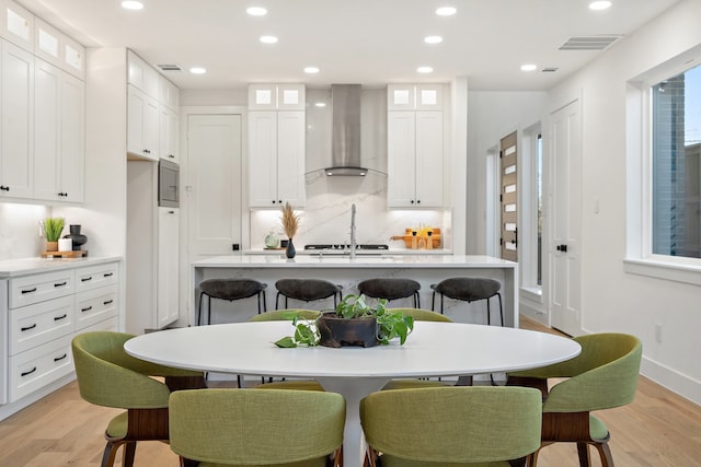 kitchen featuring a kitchen breakfast bar, wall chimney range hood, light hardwood / wood-style flooring, and a kitchen island