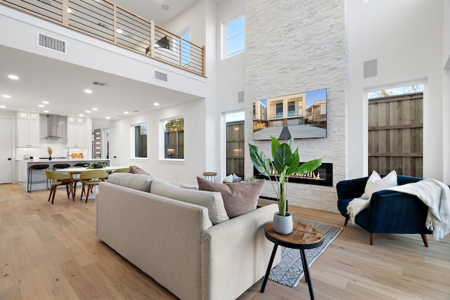 living room featuring a towering ceiling, a fireplace, a healthy amount of sunlight, and light hardwood / wood-style flooring