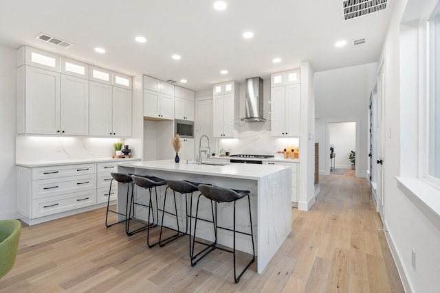 kitchen with wall chimney exhaust hood, light wood-type flooring, white cabinetry, and backsplash