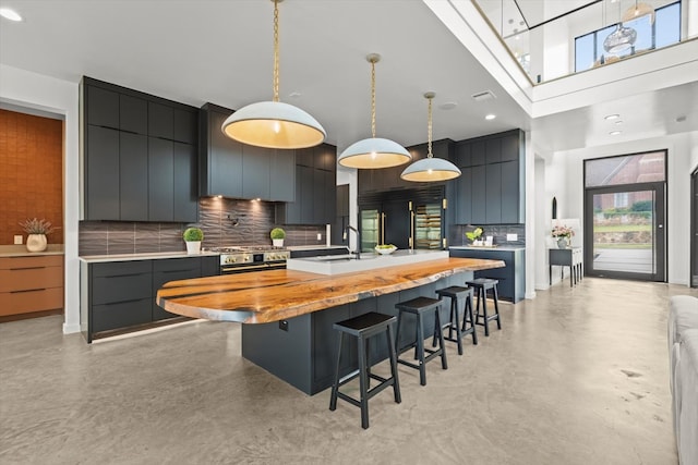 kitchen featuring a kitchen breakfast bar, tasteful backsplash, pendant lighting, stainless steel range oven, and a kitchen island with sink