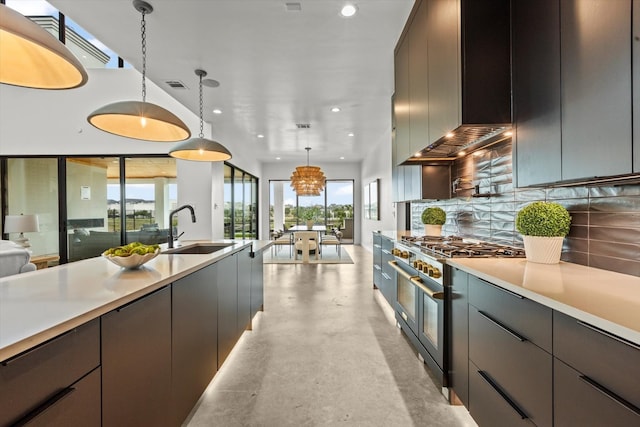 kitchen featuring wall chimney range hood, range with two ovens, pendant lighting, sink, and tasteful backsplash