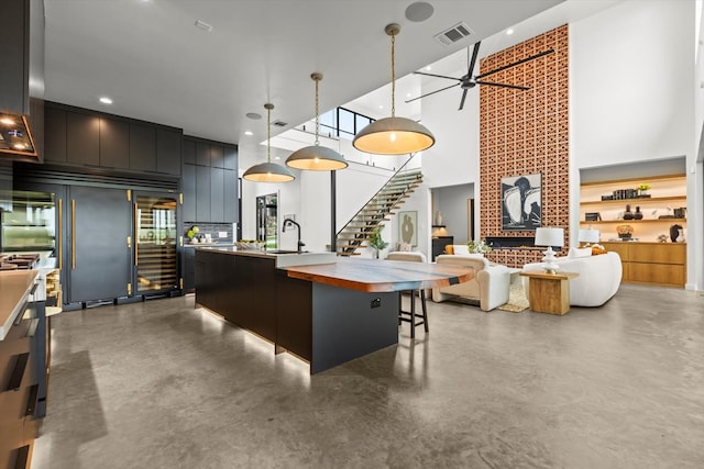 kitchen featuring a kitchen breakfast bar, a center island with sink, hanging light fixtures, ceiling fan, and concrete flooring