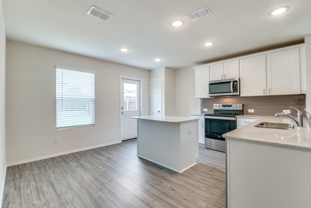 kitchen with light hardwood / wood-style flooring, stainless steel appliances, white cabinets, sink, and a center island