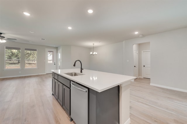 kitchen featuring dishwasher, an island with sink, sink, light wood-type flooring, and ceiling fan with notable chandelier