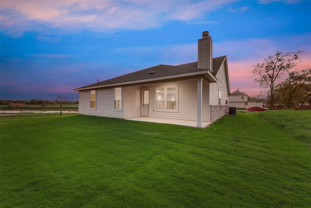 back house at dusk with a patio, central AC, and a yard