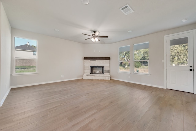 unfurnished living room featuring ceiling fan, a fireplace, light hardwood / wood-style floors, and plenty of natural light