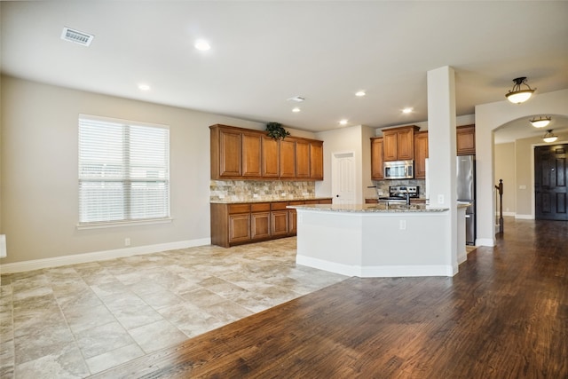 kitchen with tasteful backsplash, stainless steel appliances, light tile floors, and light stone countertops