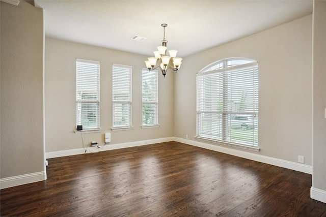 unfurnished room with a wealth of natural light, dark wood-type flooring, and an inviting chandelier