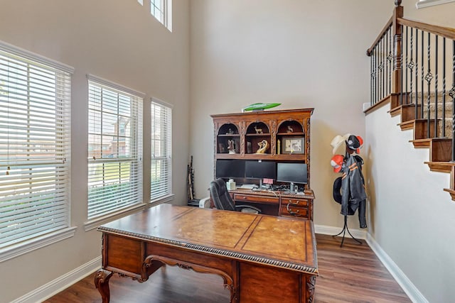 office with dark wood-type flooring, a healthy amount of sunlight, and a high ceiling