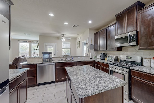 kitchen with light tile patterned flooring, a kitchen island, appliances with stainless steel finishes, sink, and dark brown cabinetry