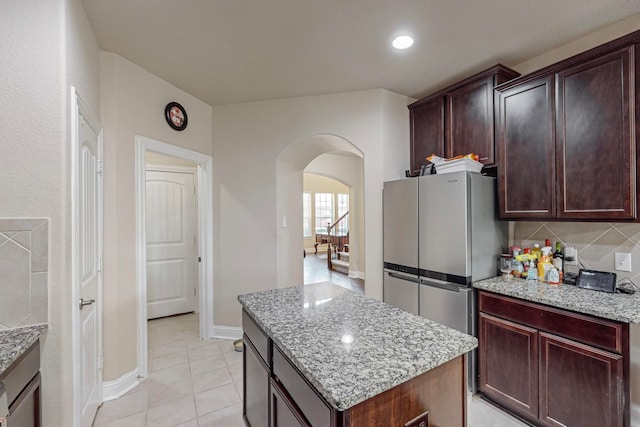 kitchen featuring stainless steel refrigerator, light stone counters, backsplash, and a kitchen island