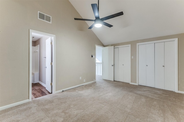 unfurnished bedroom with ensuite bathroom, two closets, ceiling fan, light colored carpet, and high vaulted ceiling