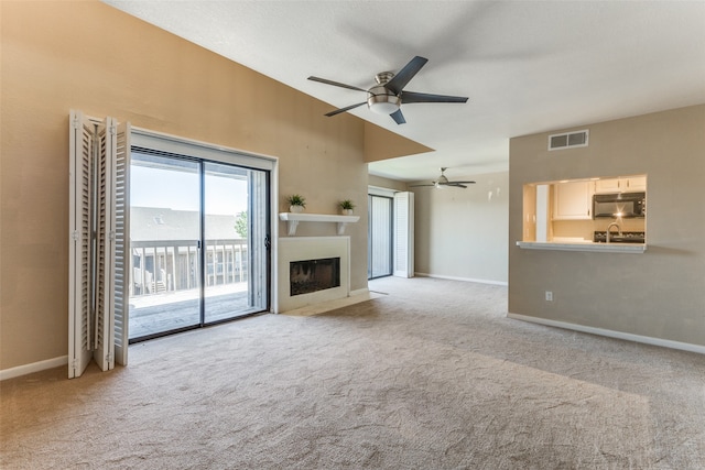 unfurnished living room featuring ceiling fan, light colored carpet, and sink